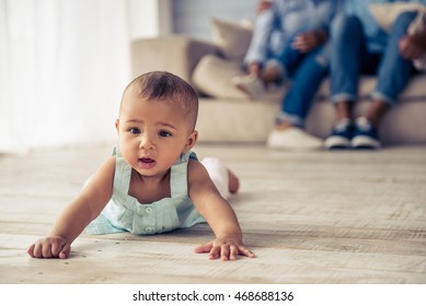 Adorable Afro American baby girl is looking forward with interest while crawling on wooden floor at home