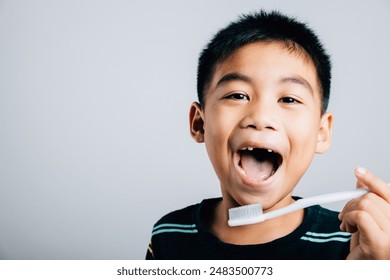 An adorable Asian boy missing an upper milk tooth holds a toothbrush showcasing dental care routine and the happiness of learning. Isolated on white background. Children dentist routine - Powered by Shutterstock