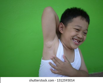 An Adorable Asian Boy Wearing A White Top. He's Smiling Widely And Showing His Arm Pit.