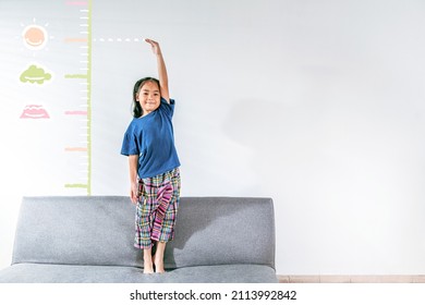 An Adorable Asian Little Child Girl Measuring The Height Growth With The Imagination Drawing On The White Wall Background. Girl Power Future And Dream Concept Idea. Copy Space.