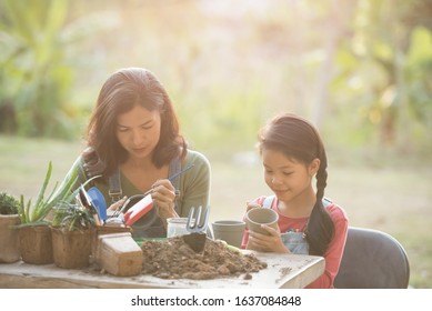 Adorable Asian Little Girl Are Painting Potted Plants Made Of Pottery In Garden Outside House, Caring For New Life. Earth Day Holiday Concept. World Environment Day. Ecology.