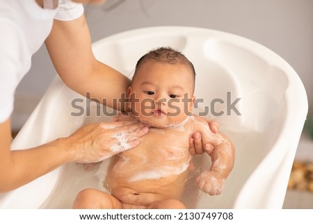 Adorable of asian newborn baby bathing in bathtub.mother bathing her son in warm water.Happy adorable newborn infant smile in tub relax and comfortable.Newborn baby care concept