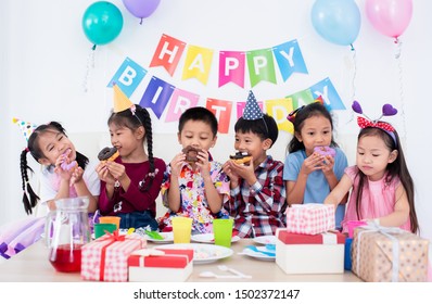 Adorable Asian Schoolkids Group Enjoy The Birthday Party At Home Many Gift Boxes, Happy Children Boys , Girls Kids Eating Bakery Doughnuts  And Drink Juice Together With Cheerful In Recreation Parties