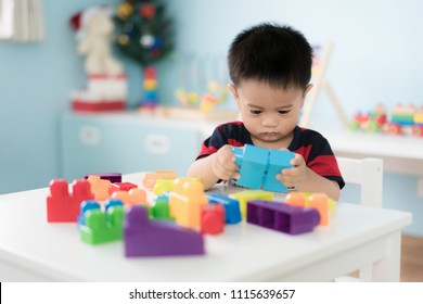 Adorable Asian Toddler Baby Boy Sitting On Chair And Playing With Color Block Toys At Home.
