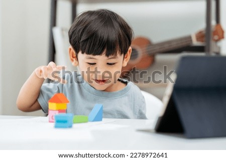 Adorable Asian Toddler baby boy sitting on chair and playing with color block toys at home.