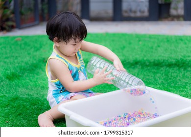 Adorable Asian Toddler Boy Playing With Sensory Water Bead. Cute Child Pours A Plastic Bottle, Pouring Orbiting Into A White Basin. The Little Ones Are Learning Science By Playing. Child Boy 2 Years.