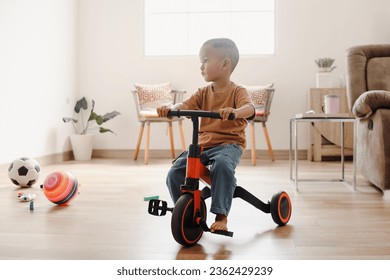 Adorable Asian toddler riding on tricycle at home and looking aside. 