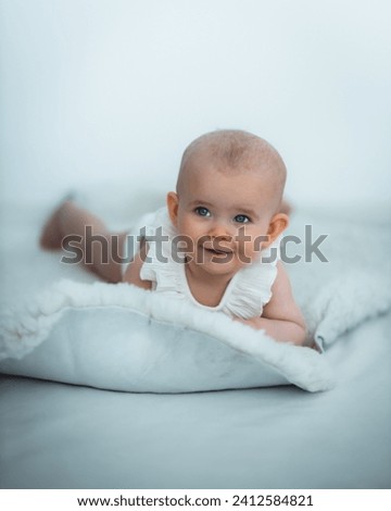 Adorable baby with beaming smile lying on soft white blanket, wearing pristine white clothing