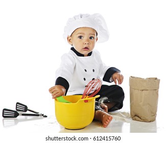 An adorable baby boy dressed as a chef and sitting among baking equipment and flour.  On a white background.