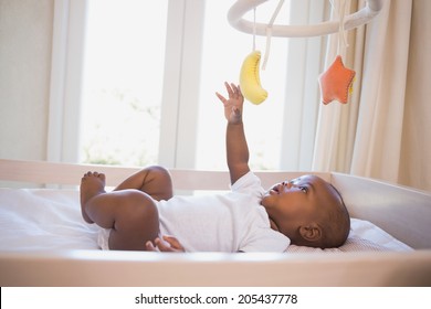 Adorable baby boy lying in his crib playing with mobile at home in the bedroom