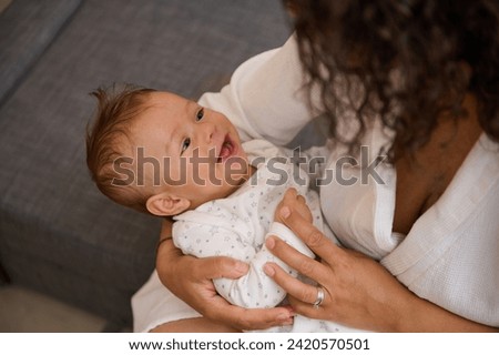 Adorable baby boy nestling in his mother's arms, smiles looking at his mom stroking, kissing, embracing and cuddling him. Young affectionate loving caring mother enjoys happy moments with her child