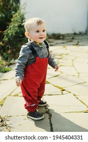 Adorable Baby Boy One Year Old In Red Waterproof Trousers Walking Outside On Sunny Spring Day