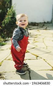 Adorable Baby Boy One Year Old In Red Waterproof Trousers Walking Outside On Sunny Spring Day