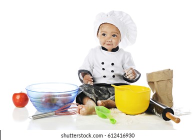 An adorable baby boy playing chef in a chef's outfit, backing equipment, apples and flour. On a white background.