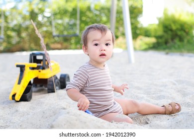 Adorable Baby Boy Playing With Sand On Outdoor Playground. Happy Mixed Race Asian-German Child Having Fun With Excavator, Truck Toys In The Summer.