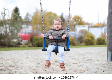 Adorable baby boy swinging on a swing at outdoor playground. Mixed race Asian-German infant having outside.kid wearing warm jacket in autumn fall season.