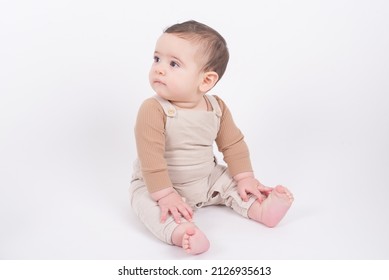 Adorable baby boy wearing beige overalls sitting on white background looking at camera and smiling.  - Shutterstock ID 2126935613