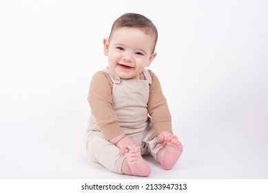 Adorable baby boy wearing beige overalls sitting on white background looking at camera and smiling.  - Shutterstock ID 2133947313