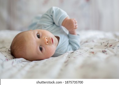 Adorable baby boy in white sunny bedroom in winter morning. Newborn child relaxing in bed. Family morning at home. Newborn kid during tummy time smiling happily at home