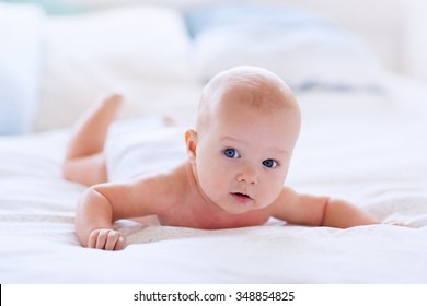 Adorable baby boy in white sunny bedroom. Newborn child relaxing in bed. Nursery for young children. Textile and bedding for kids. Family morning at home. New born kid during tummy time in a diaper.