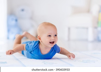 Adorable baby boy in white sunny bedroom. Newborn child relaxing on a rug. Nursery for young children. Furniture, textile and bedding for kids. New born kid during tummy time with toys at a window.