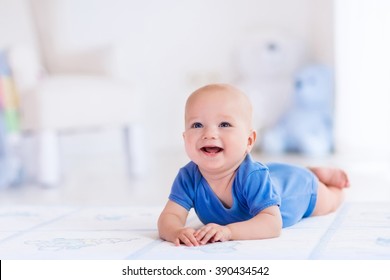 Adorable baby boy in white sunny bedroom. Newborn child relaxing on a rug. Nursery for young children. Furniture, textile and bedding for kids. New born kid during tummy time with toys at a window.