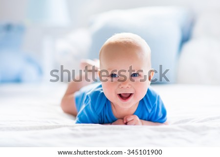 Adorable baby boy in white sunny bedroom. Newborn child relaxing in bed. Nursery for young children. Textile and bedding for kids. Family morning at home. New born kid during tummy time with toy bear.