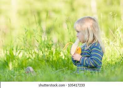 Adorable baby eat banana sitting on grass in park