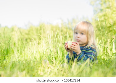 Adorable baby eat red apple sitting on grass in park