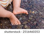 Adorable baby feet soaking in clear water over colorful rocks on a summer day in Waterton, Alberta, Canada, capturing the essence of childhood and nature.