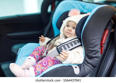 Adorable Baby Girl With Blue Eyes Sitting In Car Seat. Toddler Child In Winter Clothes Going On Family Vacations And Jorney