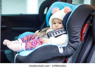 Adorable Baby Girl With Blue Eyes Sitting In Car Seat. Toddler Child In Winter Clothes Going On Family Vacations And Jorney