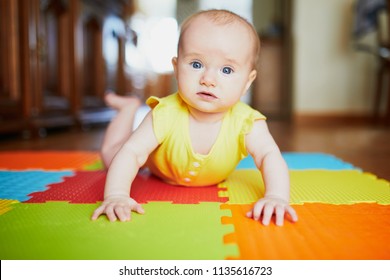 Adorable baby girl doing tummy time on colorful play mat