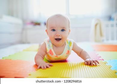 Adorable baby girl doing tummy time on colorful play mat. Happy healthy kid playing on the floor