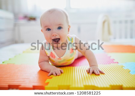 Adorable baby girl doing tummy time on colorful play mat. Happy healthy kid playing on the floor