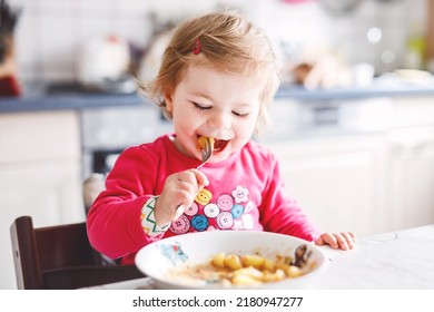 Adorable Baby Girl Eating From Fork Vegetables And Pasta. Food, Child, Feeding And Development Concept. Cute Toddler, Daughter With Spoon Sitting In Highchair And Learning To Eat By Itself.