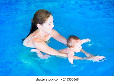 Adorable baby girl enjoying swimming in a pool with her mother, early development class for infants teaching children to swim and dive