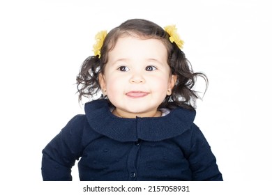 Adorable Baby Girl In A Headshot Over White Background. She Is Making Funny Faces To Her Mom