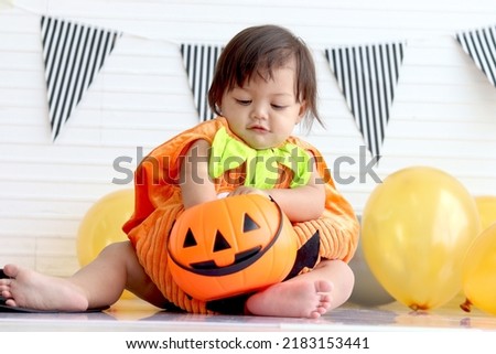 Adorable baby girl kid dressing up in orange fancy Halloween pumpkin costume, cheerful little cute child go to party, playing trick or treat, Happy Halloween celebration.