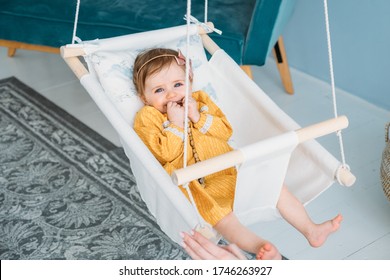 Adorable baby girl lying in a linen handmade swing. Scandinavian interior in modern apartment. House decor, cozy handmade toys, desing of kids room.