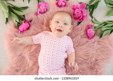 Adorable baby girl lying on fluffy rug with flowers, top view