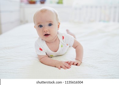 Adorable baby girl lying on bed and doing tummy time in nursery