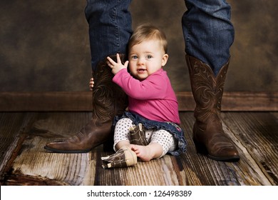 Adorable baby girl sitting on the floor holding her mothers leg.