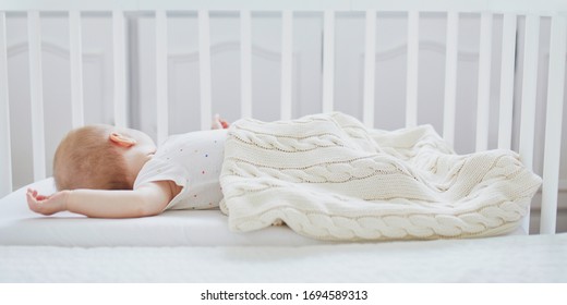 Adorable Baby Girl Sleeping In Co-sleeper Crib Attached To Parents' Bed. Little Child Having A Day Nap In Cot. Sleep Training Concept. Infant Kid In Sunny Nursery