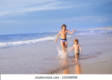 Adorable Baby Girl Wearing A Diaper And Her Brother Running Together On A Beautiful Beach Splashing Water