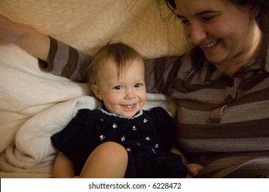 Adorable baby laughing and looking at the viewer as her mother is lifting up a blanket made into a tent fort.