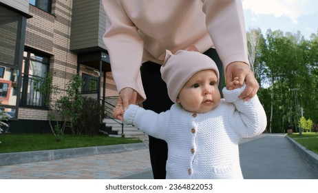 Adorable baby learning to walk with help of mother outdoors - Shutterstock ID 2364822053
