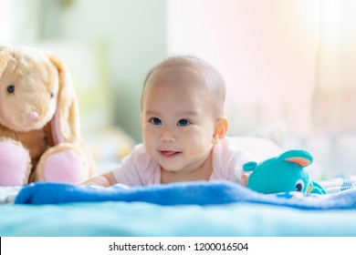 Adorable baby on bedroom on morning. Newborn 5 months child relaxing in bed. New born kid during tummy time with stuffed animal toys.