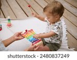 An adorable baby playing a colorful xylophone with the support of a parent, enjoying playful and musical moments outdoors on a cozy blanket.