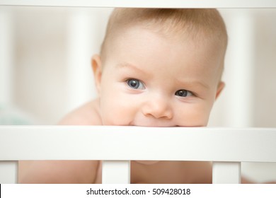 Adorable Baby Smiling And Biting The Board Of His Wooden Cot, Teething Process. Family, Home Concept Photo, Close Up